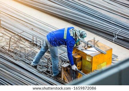 Selective focus to construction worker and many deformed steel bar working with electric iron cutting machine at the construction site. Large scale high rise building construction project. Royalty-Free Stock Photo #1659872086