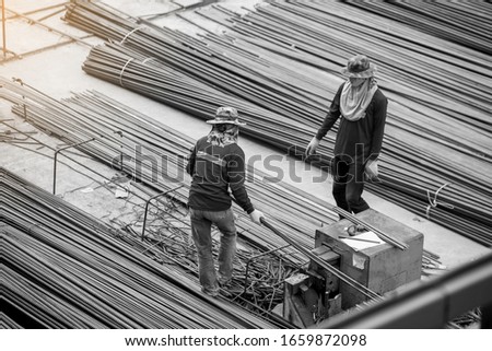 Black and white imahe of construction worker and many deformed steel bar working with hydraulic rebar cutting machine at the construction site. Large scale high rise building construction project. Royalty-Free Stock Photo #1659872098
