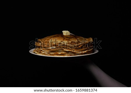 Pancakes with a piece of butter on a white plate on a black background