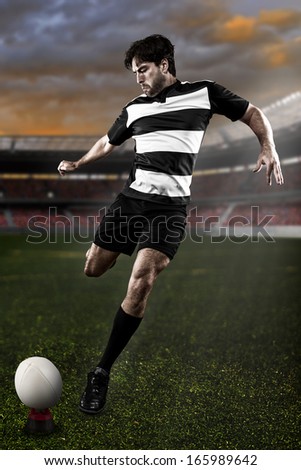 Rugby player in a black and white uniform kicking on a stadium.