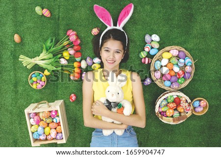 Portrait of cute little girl holding a rabbit doll lying on the grass with an easter-painted egg in rattan basket and on grass. Happy easter day concept