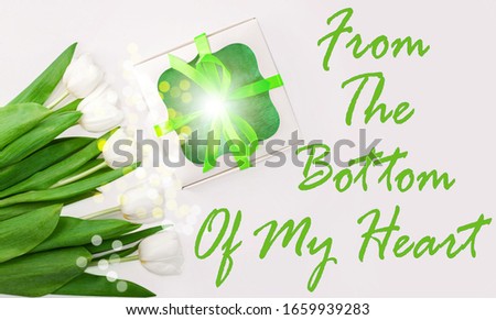 From The Bottom Of My Heart text message sign on light background.White tulip flowers and gift box with green ribbon bow flat lay.Flower Bouquet congratulations greeting card.Copy space website banner