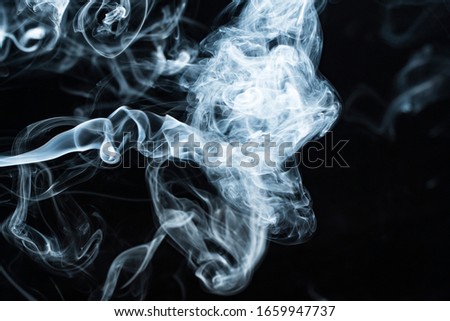 Background image of a wisp of smoke on a dark background. The texture of the flowing smoke. Frozen smoke on a dark background. Texura of white clouds of fog. Curls of smoke frozen in motion.