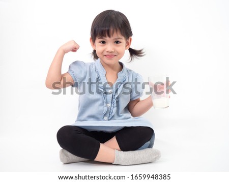 Asian little cute girl 4 years old holding and drinking milk from glasses and raising her arm to be strong on white background. Milks is essential and nutrition for the child's body. Royalty-Free Stock Photo #1659948385