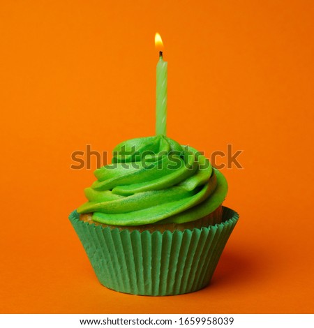 Delicious birthday cupcake with green cream and burning candle on orange background