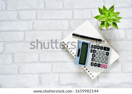 Top view objects , calculator, black pen on  notebook  with small cactus green leave  white gray brick background. Idea home loan background or home finance concept. sensitive focus.