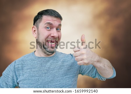 cheerful charismatic bearded young man with no front upper teeth gives a thumbs up, thumb gesture all is well, funny toothless bearded young man Royalty-Free Stock Photo #1659992140