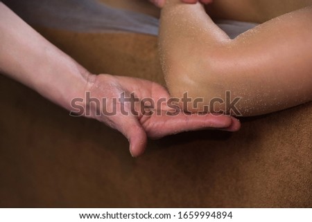 Massagist man scrubbing woman's shoulder, arm with natural scrub in spa salon. Procedure of peeling and massaging body for young girl in cosmetology clinic, hands closeup. Skincare bodycare concept. Royalty-Free Stock Photo #1659994894