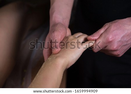 Massagist man scrubbing woman's hand and fingers natural scrub in spa salon. Procedure of peeling and massaging body for young girl in cosmetology clinic, hands closeup. Skincare bodycare concept. Royalty-Free Stock Photo #1659994909
