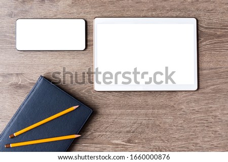 Blue-black day planner with leather cover and two pencils on it. Smartphone and tablet with white blank screens on a wooden background. Preparation for the business meeting. Space for text or a logo.