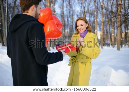 guy giving gift to lovely girlfriend outdoors. man and woman on romantic date, male came with red gift box. happy lady in green coat emotionally reacts to gift. love, saint valentines day concept