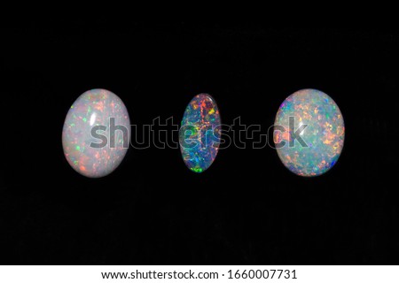 Close up of three colourful and precious Queensland opals including two white and a rare black opal to make quality and expensive jewelry. Gemstone opals give beautiful coloured flashed of light.
