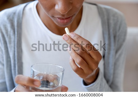 Close up of African American young woman feel sick drink antibiotic or antidepressant pill with water, biracial female suffer from illness take prescribed medicines or tablet, healthcare concept Royalty-Free Stock Photo #1660008004
