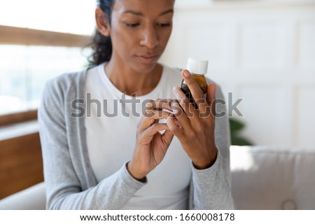 Young African American woman hold medication bottle reading instruction or prescription on packaging, millennial biracial female prepared to take medicine syrup, healthcare, pharmacy concept Royalty-Free Stock Photo #1660008178