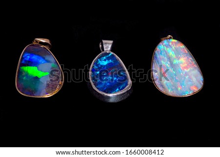 Three different colours of Queensland boulder opal made into beautiful and expensive pendant jewelry set in gold and silver showing off the gorgeous colours and refraction on a black background.