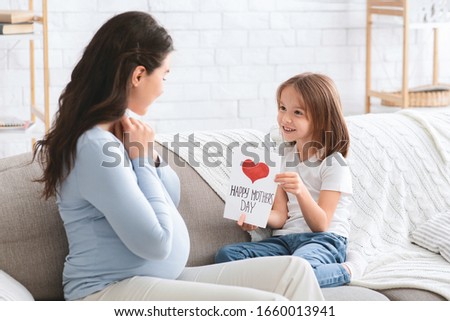 Surprised pregnant woman and her little cheerful daughter celebrating Mother's Day together at home