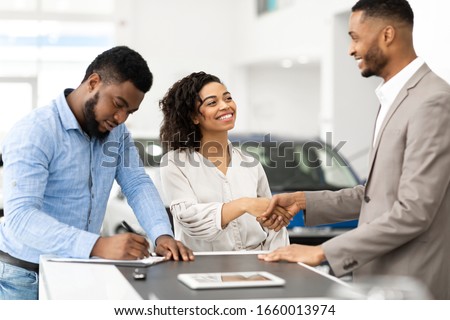 Buying Car. Black Couple Shaking Hands With Salesman And Signing Papers In Cars Selling Center. Selective Focus
