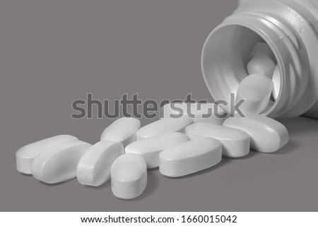 Overturned jar with oval pills on a gray background