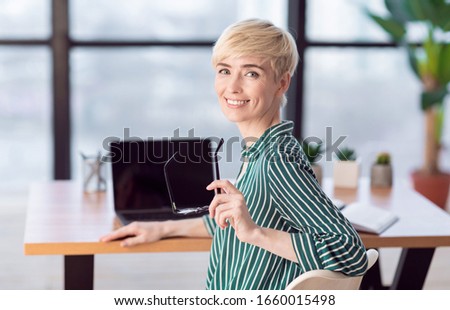 Smiling Mature Businesswoman Looking At Camera Posing Holding Eyeglasses Sitting In Modern Office. Selective Focus
