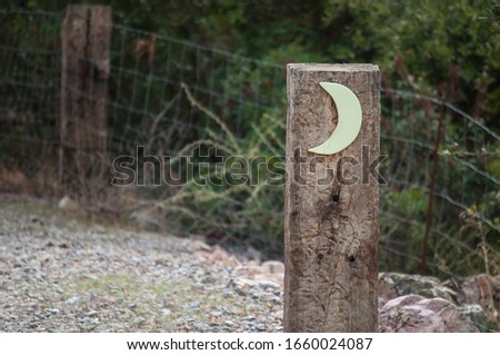 Wooden pole with drawing of a crescent in the foreground with nature behind

