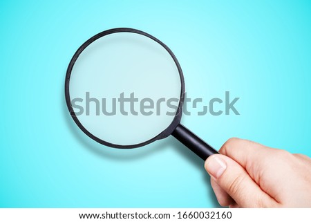 black magnifier in hand on blue background, search concept Royalty-Free Stock Photo #1660032160