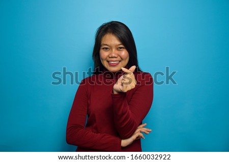 Portrait of Young beautiful asian women with blue isolated background, make love with finger