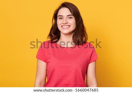 Image of attractive woman with dark hair being very glad, looking with broad smile showing her perfect teeth, excited female wearing red casual t shirt, posing isolated over yellow background. Royalty-Free Stock Photo #1660047685