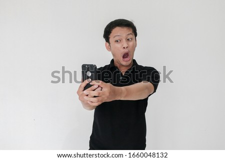 Wow face of Your Asian man shocked what he see in the smartphone on isolated grey background. Indonesia Man wear black shirt Isolated grey background.