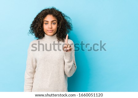 Young african american curly hair woman showing number one with finger.