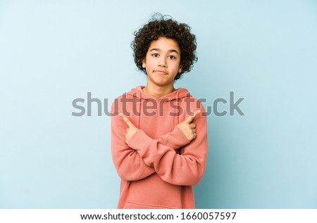 African american little boy isolated points sideways, is trying to choose between two options.