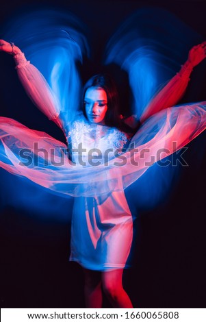 abstract portrait of a dancing girl in a dress with neon red and blue light on a dark background with a blur