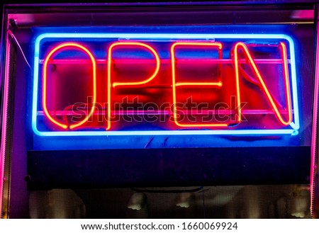 Brightly lit fluorescent sign that says open - distorted pink line reflections on the window, and lights and walls inside the store slightly visible