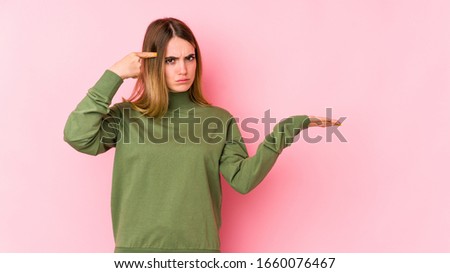 Young caucasian woman isolated on pink background holding and showing a product on hand.