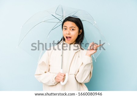 Young chinese woman holding an umbrella isolated is saying a secret hot braking news and looking aside