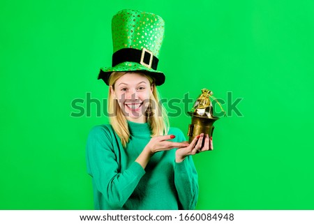 Smiling blonde girl in Leprechaun costume holds bag with gold. Green hat. Leprechaun. Bag with gold. Green leprechaun. Hat with clover. Saint Patrick's Day. Irish Traditions. Saint Patrick.