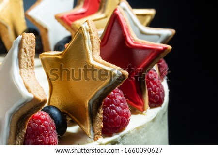 white cake with multi-colored stars blueberries and raspberries on a black background with a green ribbon. macro