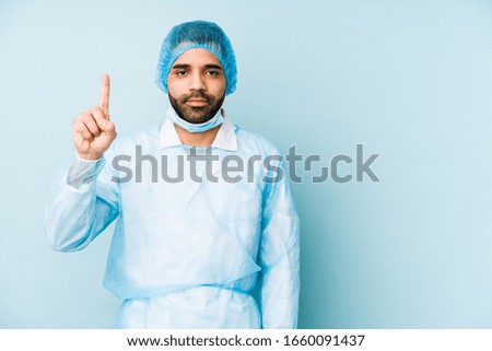 Young surgeon latin man isolated Young dshowing number one with finger.