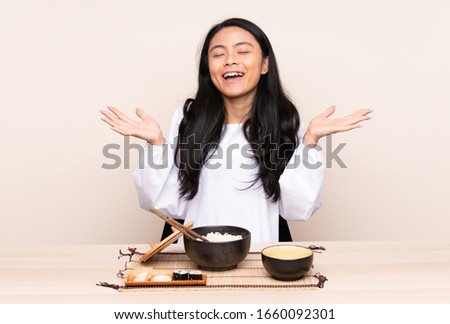 Teenager Asian girl eating asian food isolated on beige background smiling a lot