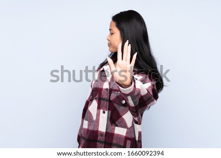 Teenager Chinese woman isolated on blue background making stop gesture and disappointed