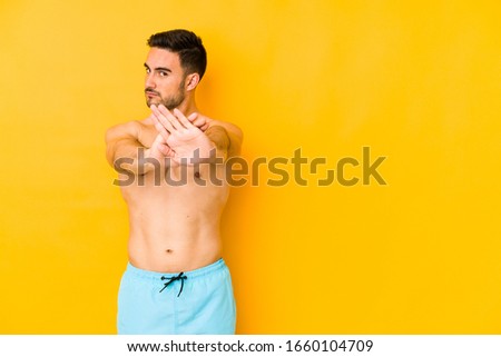 Young caucasian man with swimsuit isolated on yellow background Young caucasian man with trdoing a denial gesture