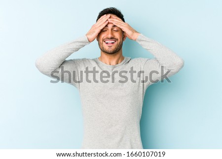 Young caucasian man isolated on blue background laughs joyfully keeping hands on head. Happiness concept.