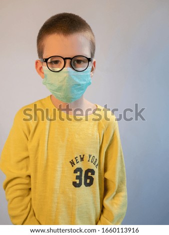 cute blonde boy in blue medical mask and glasses is quarantined at home. child coughs heavily and wears mask. concept of fight against the coronavirus epidemic and proper prevention of infections