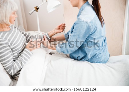 Loving granddaughter rolling up sleeves of grandmother while she lying on bed stock photo