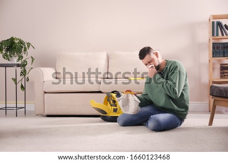 Man with vacuum cleaner bag suffering from dust allergy at home Royalty-Free Stock Photo #1660123468