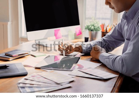 Young creative designer working with color palette samples and pen tablets. Black screen computer mockup for graphic montage.