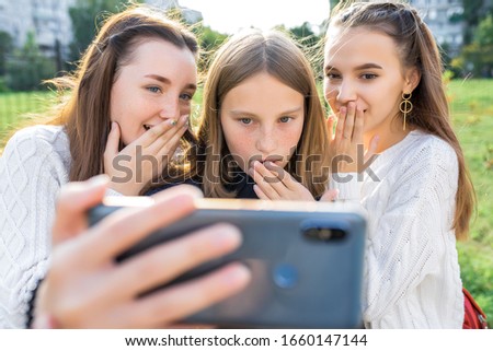 3 teenage girls watching video on phone. In summer in city. Emotions of surprise, surprise, delight, fear. Selfie photo. Video recording. Social networks, video clip on Internet. Online application
