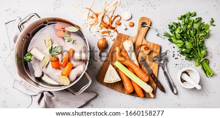 Cooking - preparing chicken stock (broth or bouillon) with vegetables in a pot. Kitchen - grey concrete worktop scenery from above (top view, flat lay).