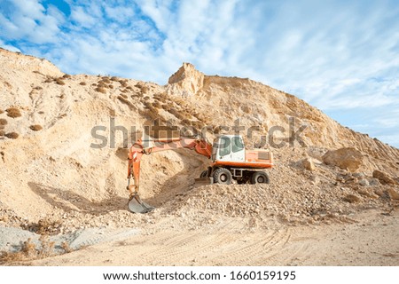 Empty inactive digger equipment sitting on dry mountainside with rocks and tire tracks