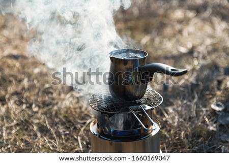 preparing coffee on portable wood burner at campsite in mountains