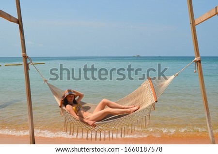 Beautiful portrait of a young woman in a straw hat lying in a cozy hammock against the sea on the beach in summer lifestyle. Atmosphere for meditation and calm mood. Concept of solitude, hygge